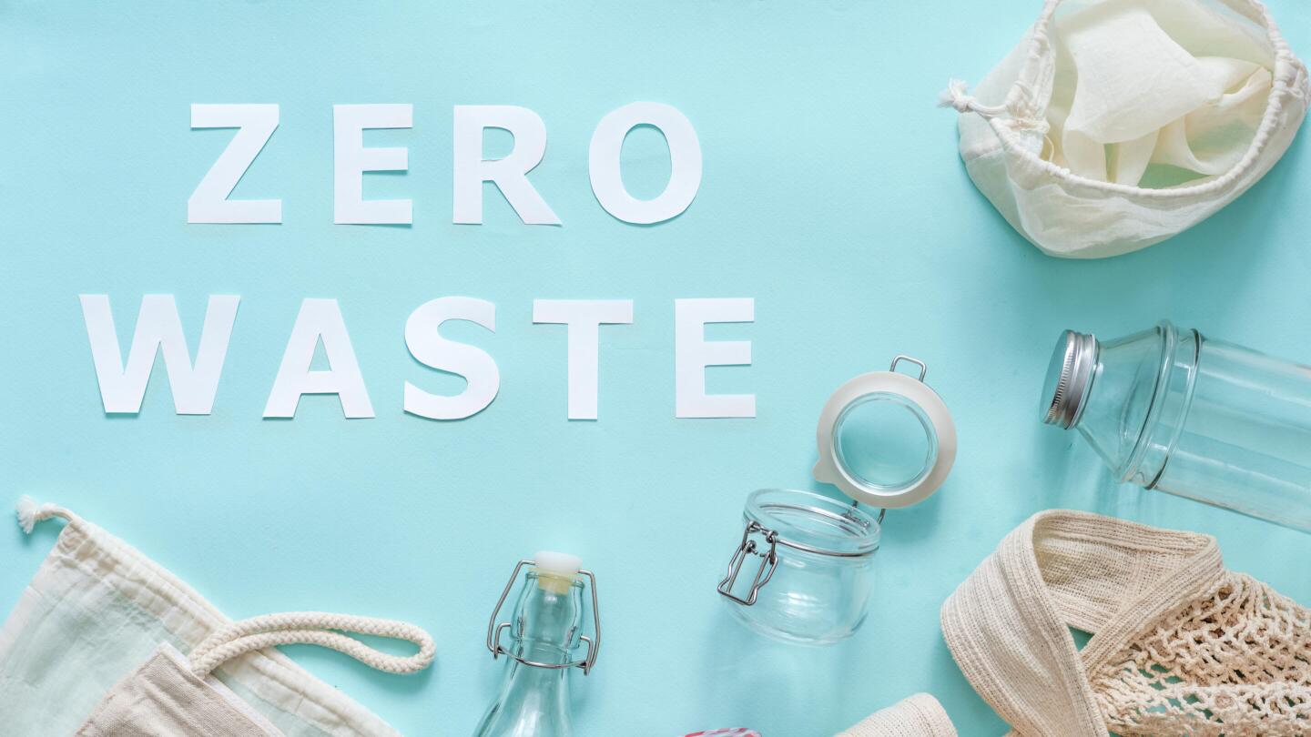 The words “ZERO WASTE” are laid out on a light blue background, surrounded by reusable glass bottles, jars, and cloth bags.